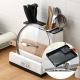 Kitchen utensil storage box with cutlery, a lid, and a cutting board on a wooden countertop.