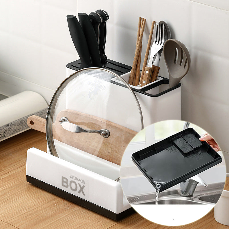 Kitchen utensil storage box with cutlery, a lid, and a cutting board on a wooden countertop.