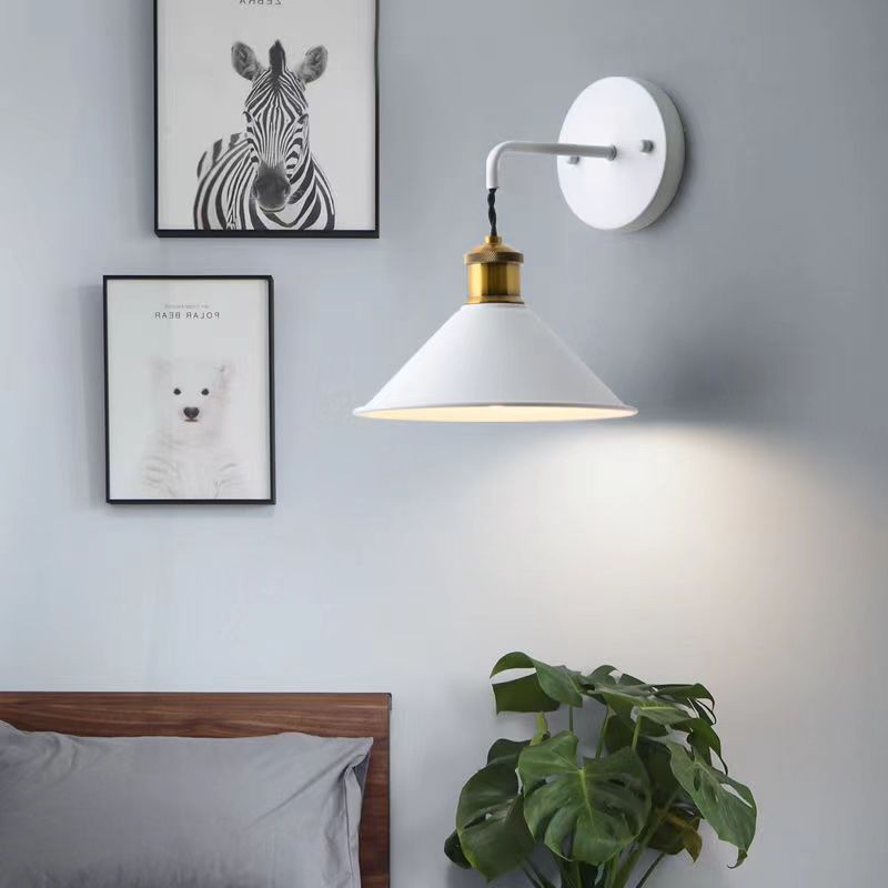 Modern wall lamp with white shade and gold base in a bedroom setting.
