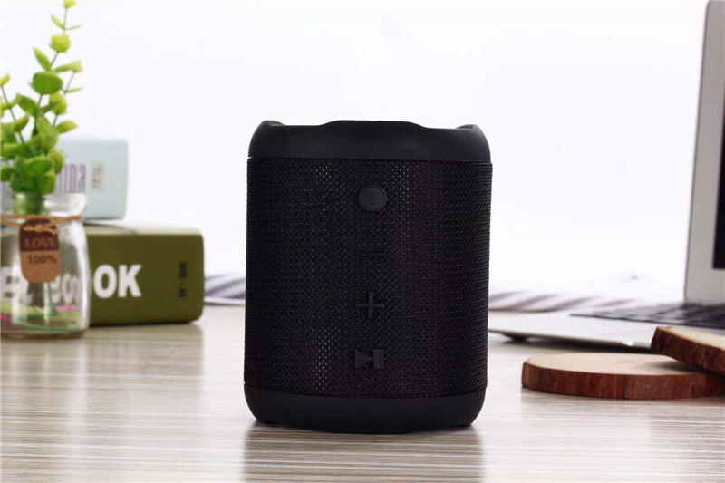 Black portable speaker on a desk with a laptop and plant in the background