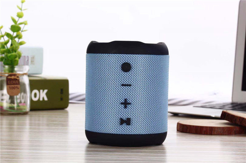 Blue portable speaker on a desk with a laptop and plant in the background
