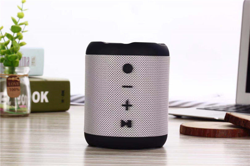 Black and white portable speaker on a desk with a laptop and plant in the background
