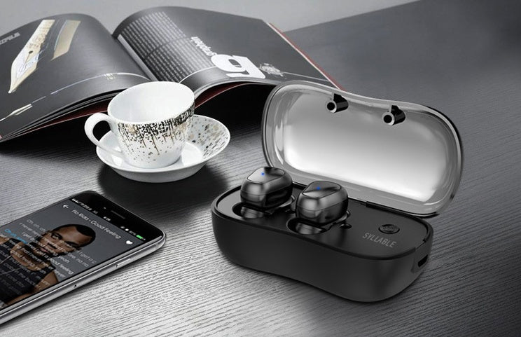 Wireless earbuds in a charging case on a table with a phone and cup in the background