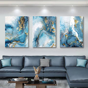 Three abstract art pieces in blue and gold on a wall above a gray sectional sofa.
