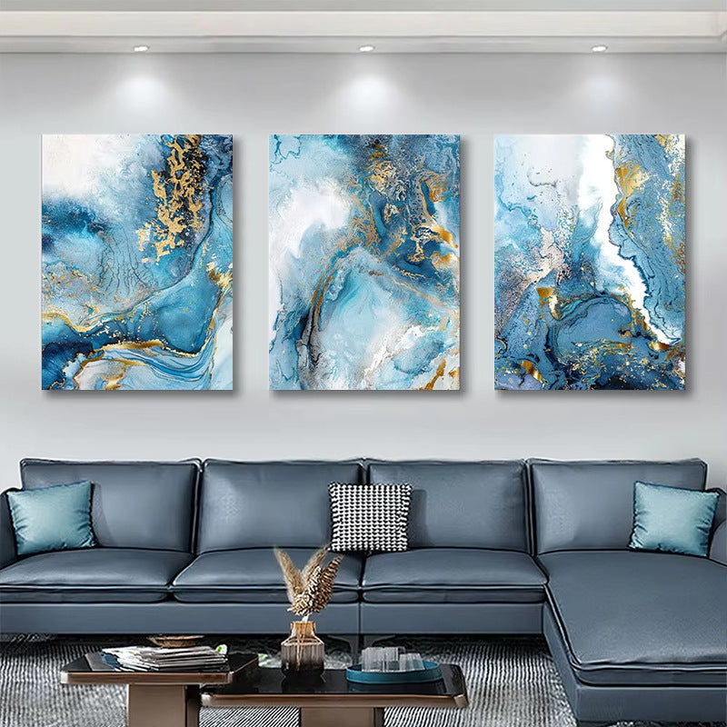 Three abstract art pieces in blue and gold on a wall above a gray sectional sofa.