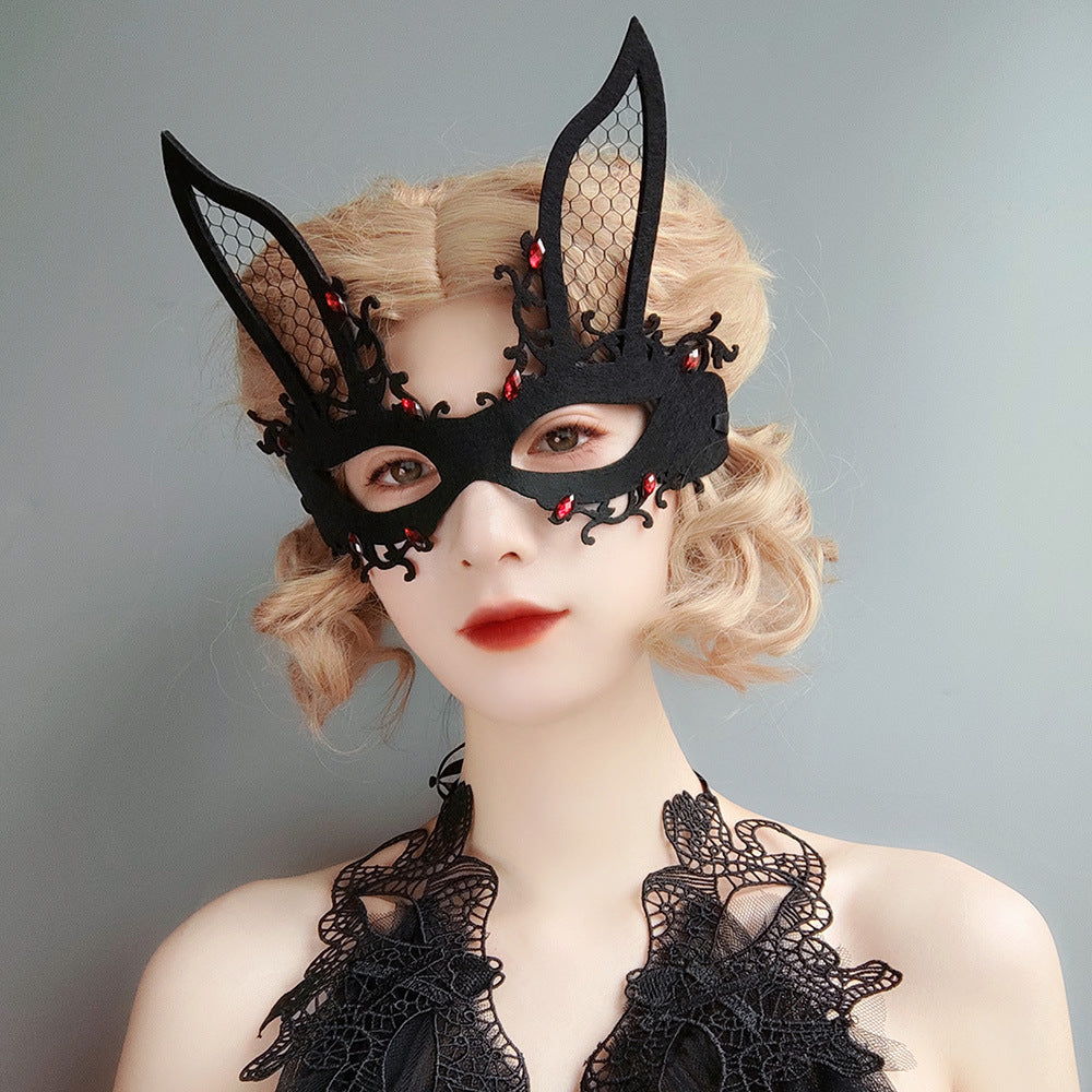 Person wearing a black lace bunny mask with red embellishments on a gray background