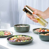 Hand holding a bottle of oil over a salad with other salads on a table.