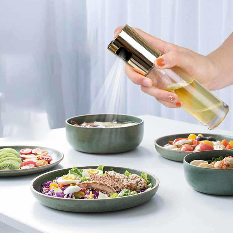 Hand holding a bottle of oil over a salad with other salads on a table.