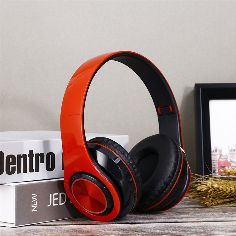 Orange and black headphones on a surface with books and a picture frame in the background.