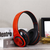 Orange and black headphones on a surface with books and a picture frame in the background.
