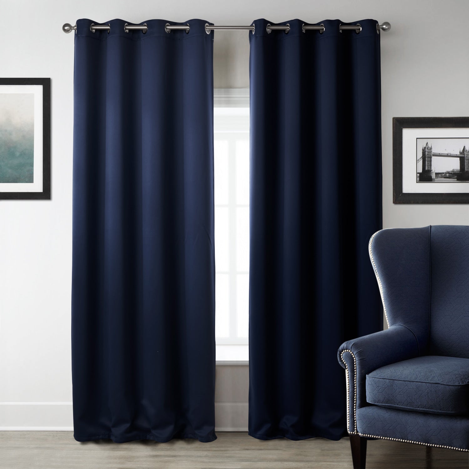 Navy blue curtains with grommets in a room with a gray chair and framed pictures.