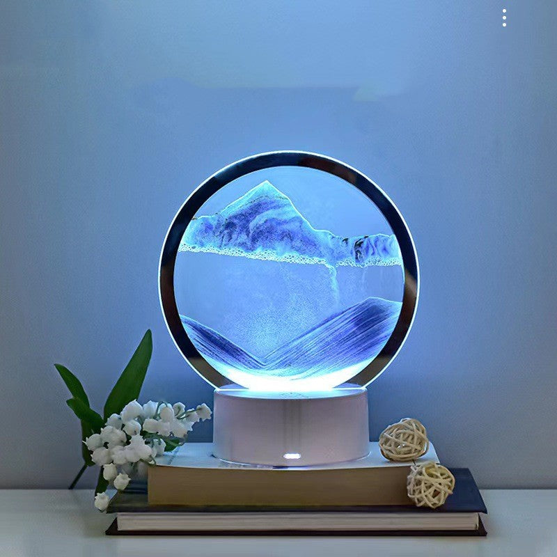 Decorative lamp with mountain and water design on a white surface with a plant and decorative ball.