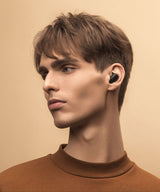 Man wearing a black wireless earbud against a beige background
