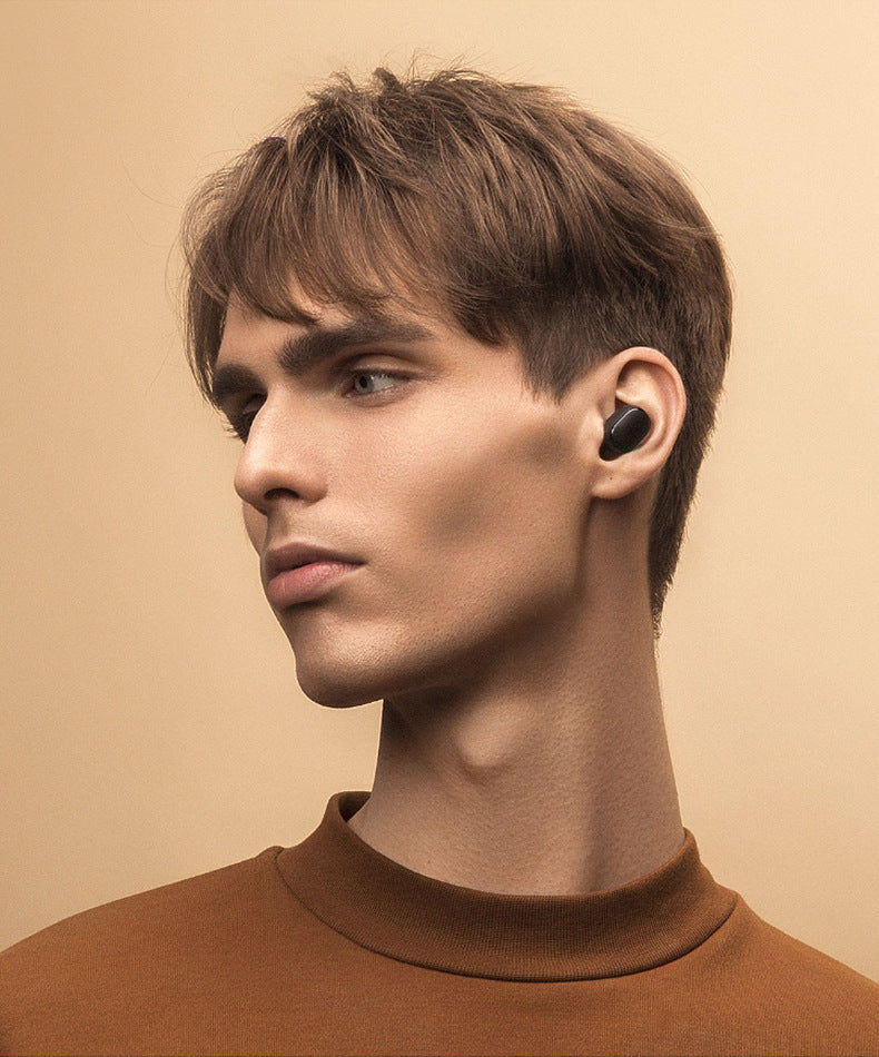 Man wearing a black wireless earbud against a beige background