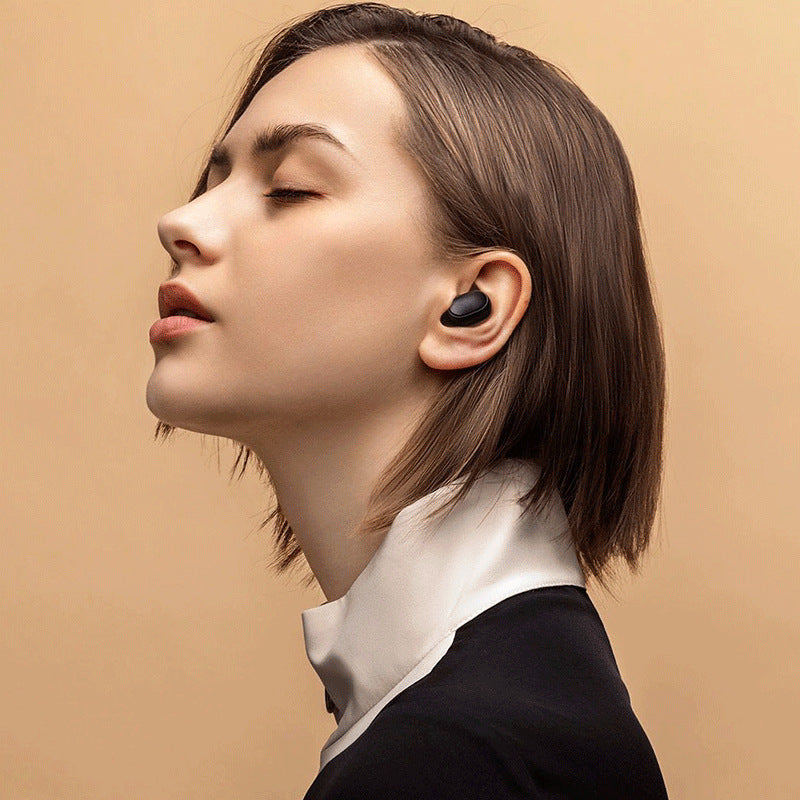 Woman wearing a black wireless earbud against a beige background