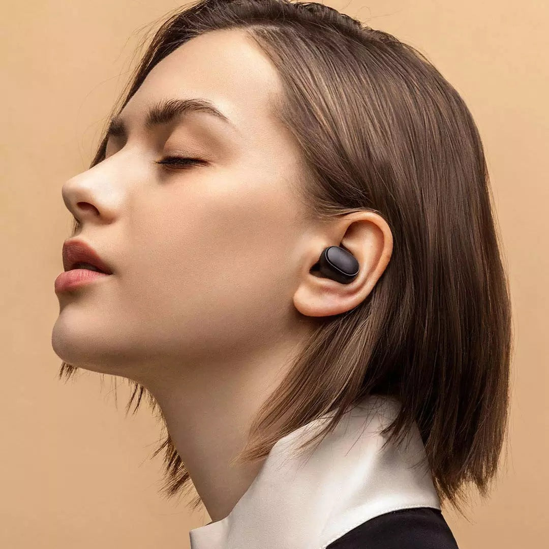 Woman wearing a black wireless earbud against a beige background