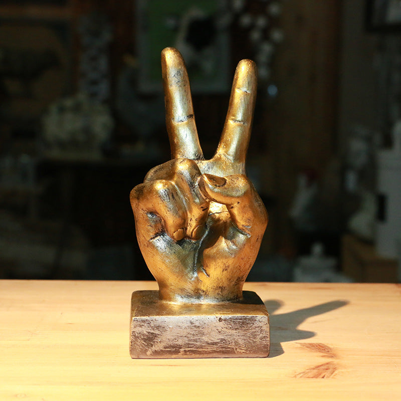 Bronze sculpture of a hand making a peace sign on a wooden surface with a blurred background
