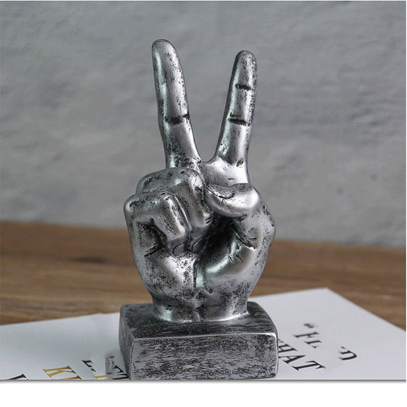 Metallic hand making a peace sign on a wooden surface with a gray background