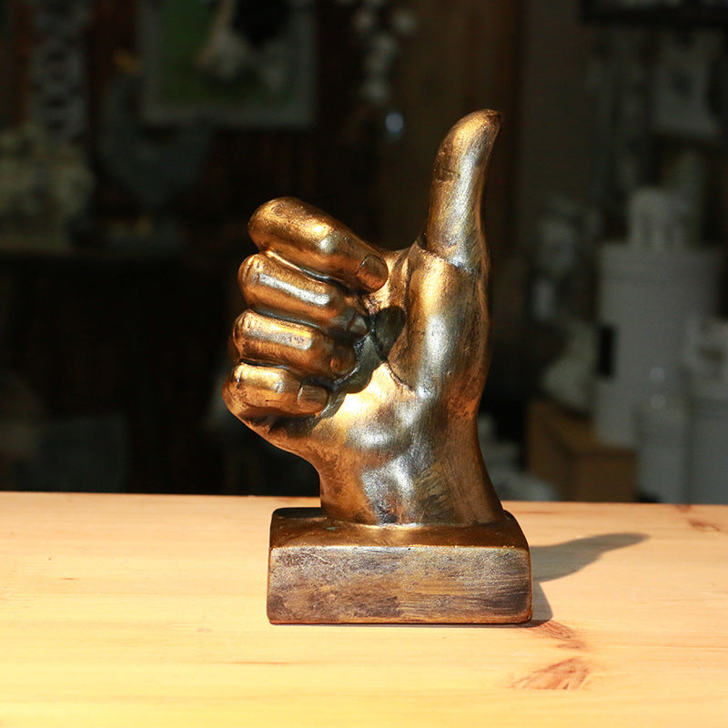 Bronze hand sculpture giving a thumbs-up gesture on a wooden surface.