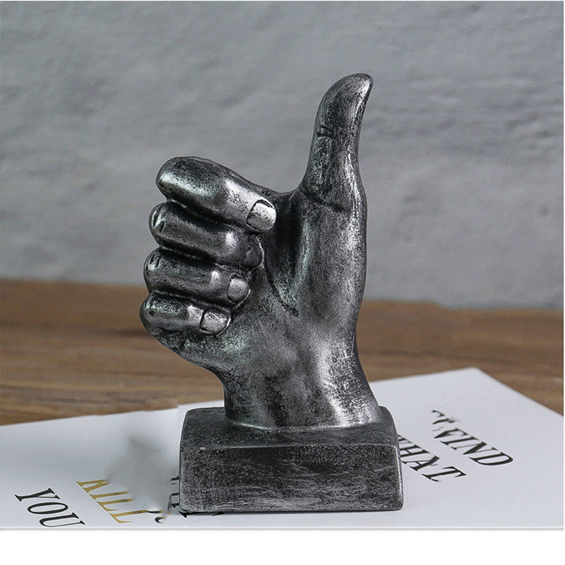 Metallic hand sculpture giving a thumbs-up gesture on a textured surface.