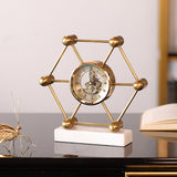 Decorative gold clock with geometric design on a white base, placed on a reflective surface.