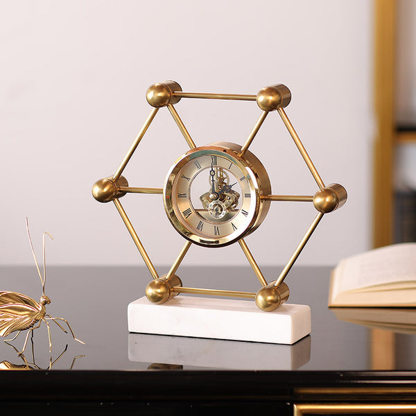 Decorative gold clock with geometric design on a white base, placed on a reflective surface.