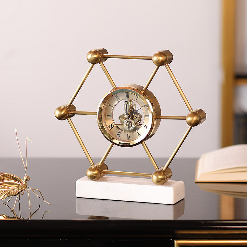 Decorative gold clock with geometric design on a white base, placed on a reflective surface.