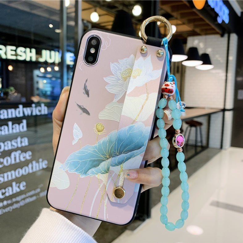Phone case with floral design held by a hand, with a beaded strap in front of a store interior.