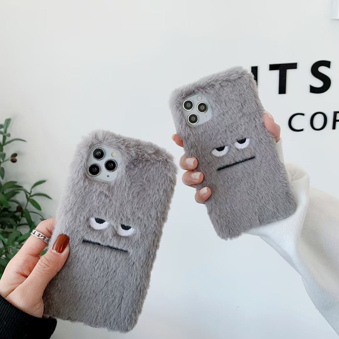 Two gray fluffy phone cases with face designs held by hands against a light background.