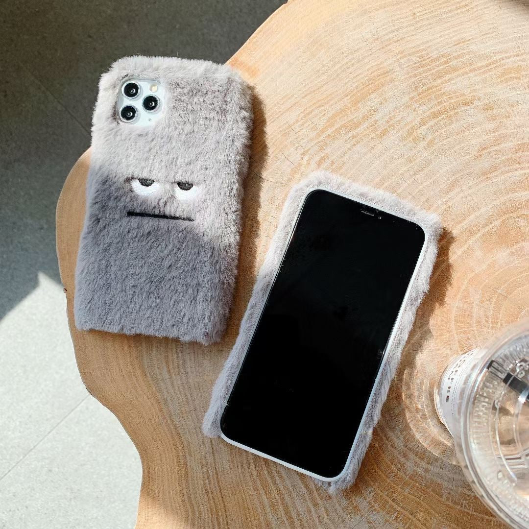 Two fluffy phone cases on a wooden surface with a glass of water.