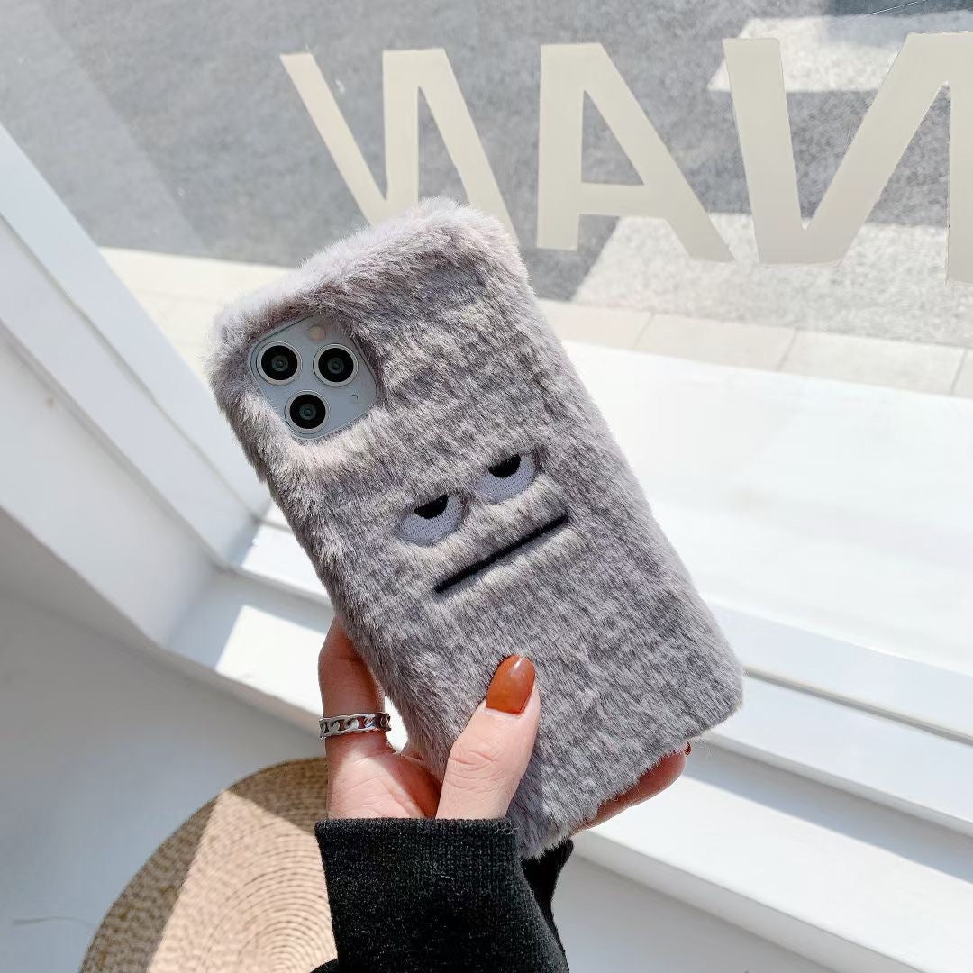 Gray textured phone case with cartoon face held by a hand against a blurred background