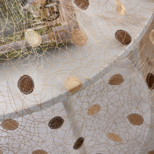 Close-up of a decorative fabric with gold thread and brown polka dots on a white background.