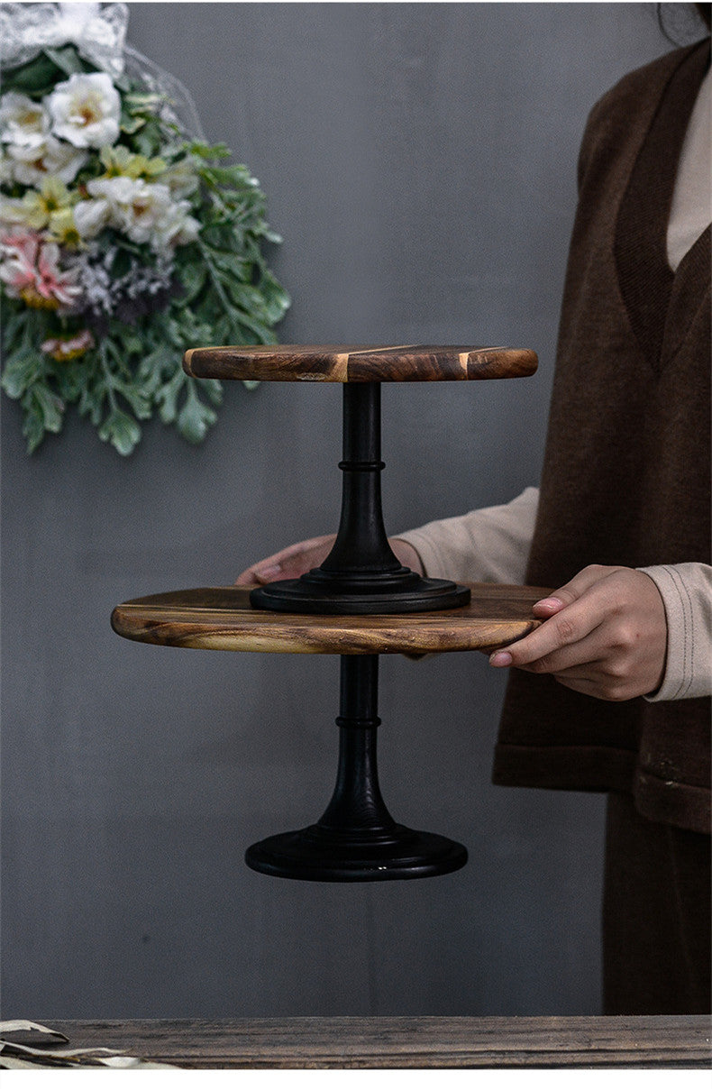 Person holding a two-tiered wooden and metal cake stand against a gray background