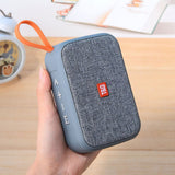Blue portable speaker with orange handle held by a hand on a wooden surface