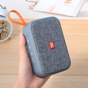 Blue portable speaker with orange handle held by a hand on a wooden surface