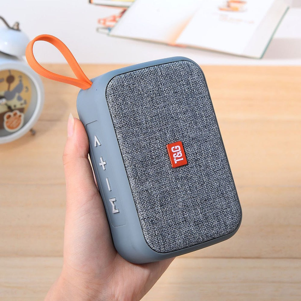 Blue portable speaker with orange handle held by a hand on a wooden surface