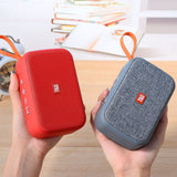Two portable speakers, one red and one gray, held in hands with a blurred background.