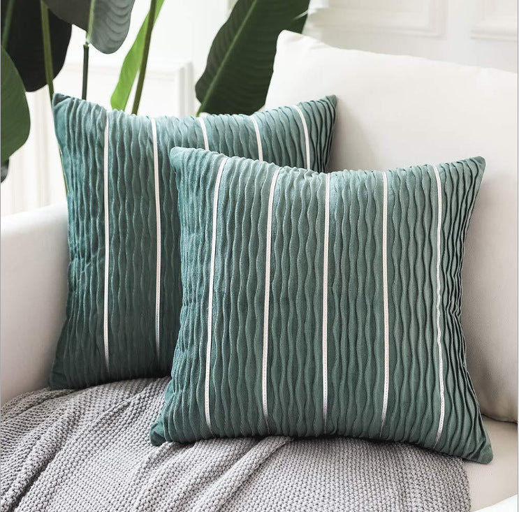 Two green striped pillows on a white couch with plants in the background