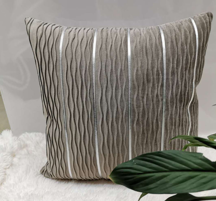 Decorative pillow with wavy pattern on a soft surface with a plant leaf.