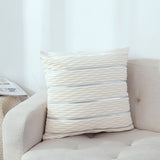 Beige pillow with horizontal stripes on a beige sofa against a white wall.