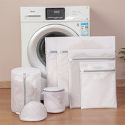 Set of laundry bags in front of a washing machine on a wooden floor.