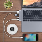 Laptop, smartphone, and coffee cup connected by USB cables on a wooden surface with a plant in the background.