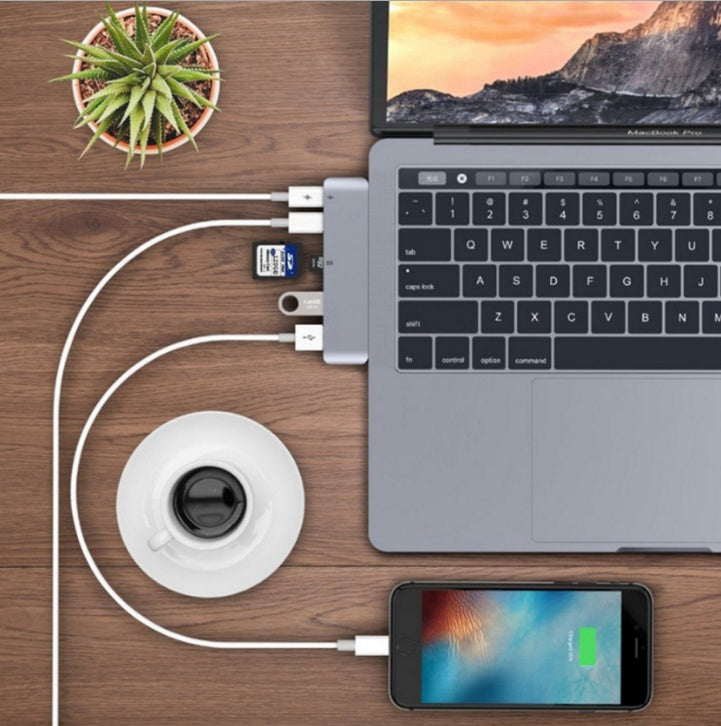 Laptop, smartphone, and coffee cup connected by USB cables on a wooden surface with a plant in the background.