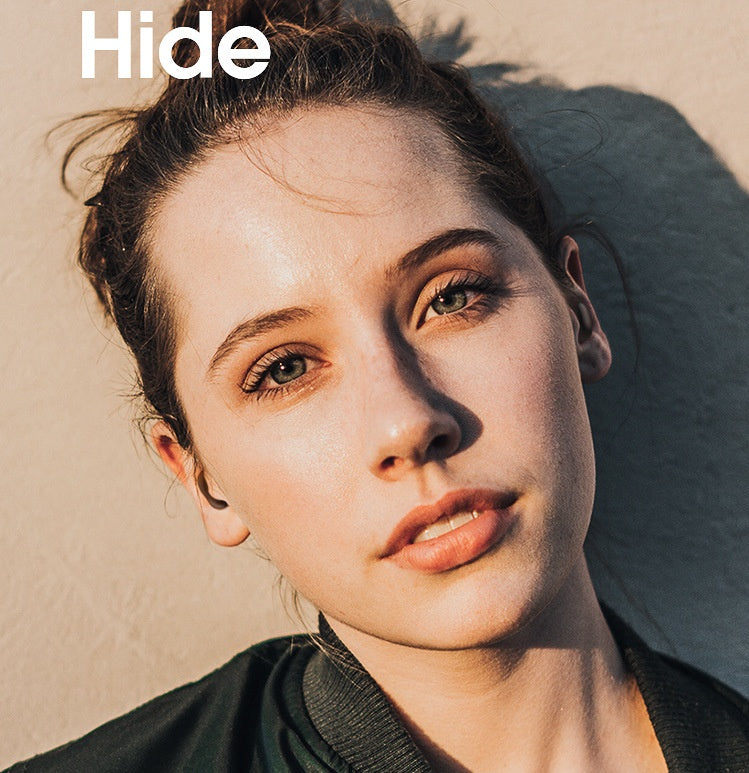 Woman lying on sand with 'Hide' logo above her head