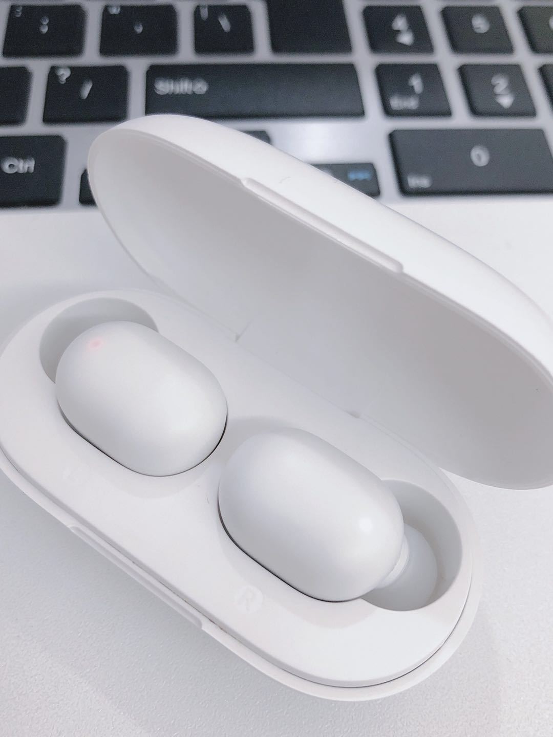 White wireless earbuds in a charging case on a laptop keyboard