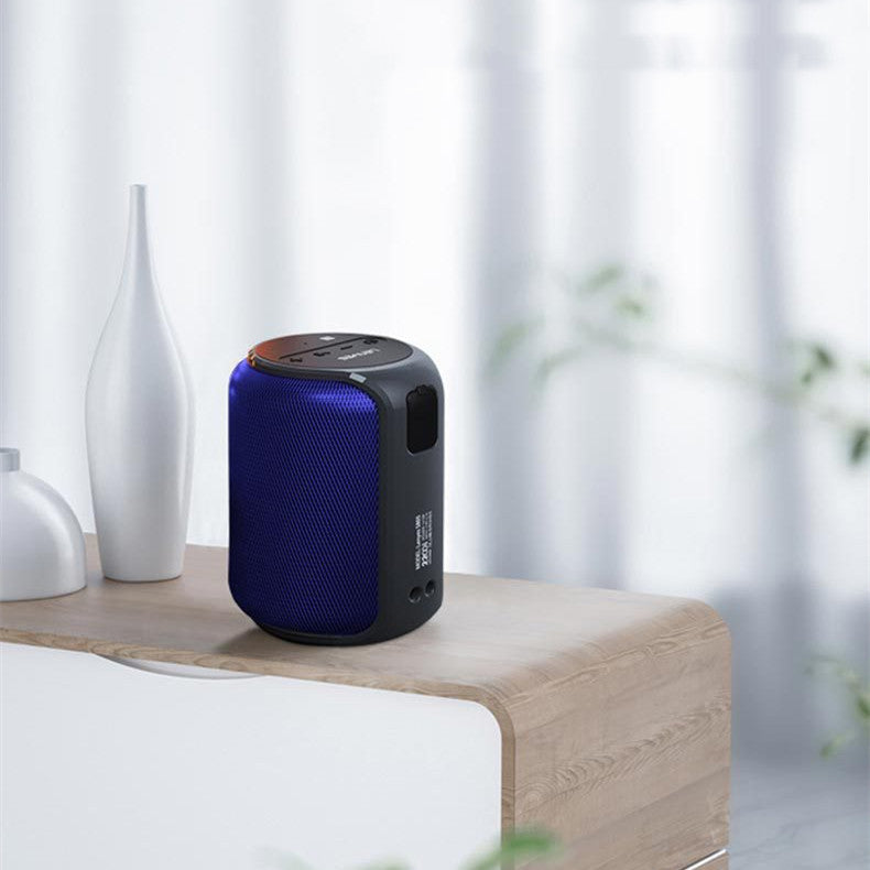 Blue and black portable speaker on a wooden surface with white vases and curtains in the background