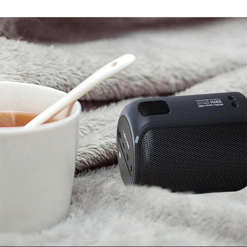 Black portable speaker on a soft surface next to a cup of tea and a toothbrush.