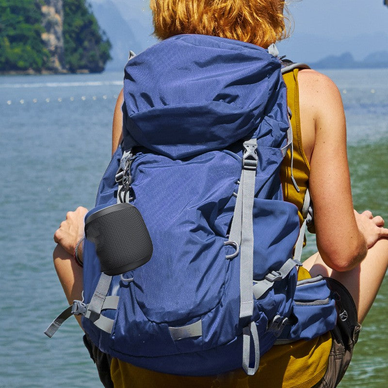 Person with a large blue backpack sitting by a body of water with mountains in the background