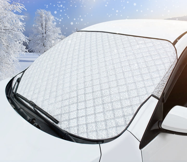 Car windshield covered with a snowflake patterned cover in a snowy landscape.