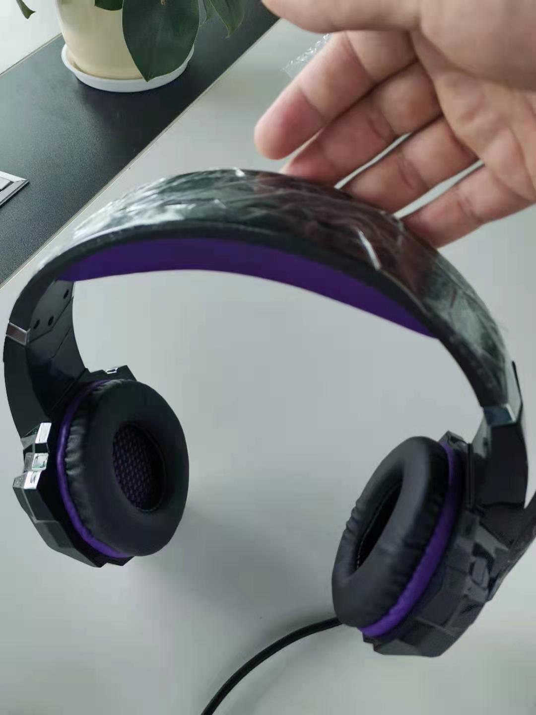Black and purple headphones on a white surface with a hand holding the headband.